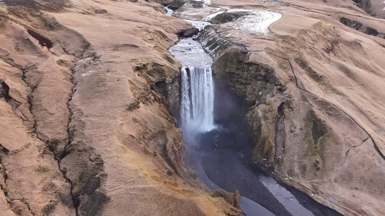 Aerial backward motion shot of Skógafoss waterfall in Skógar, Rangárþing eystra, Iceland, with the Skógá river cutting through the rugged terrain near Eyjafjallajökull.