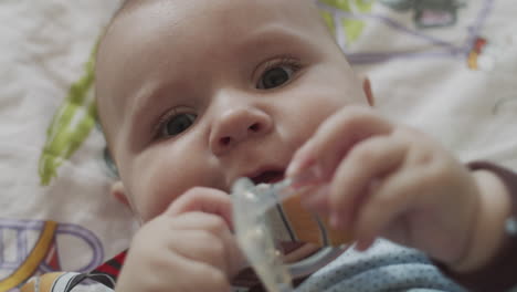 a four months old baby, lies on the coach with colorful bedsheet and playing with the baby's dummy toys, holding it in his hands