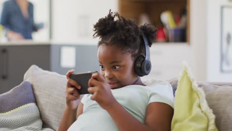 happy african american girl lying on sofa using smartphone