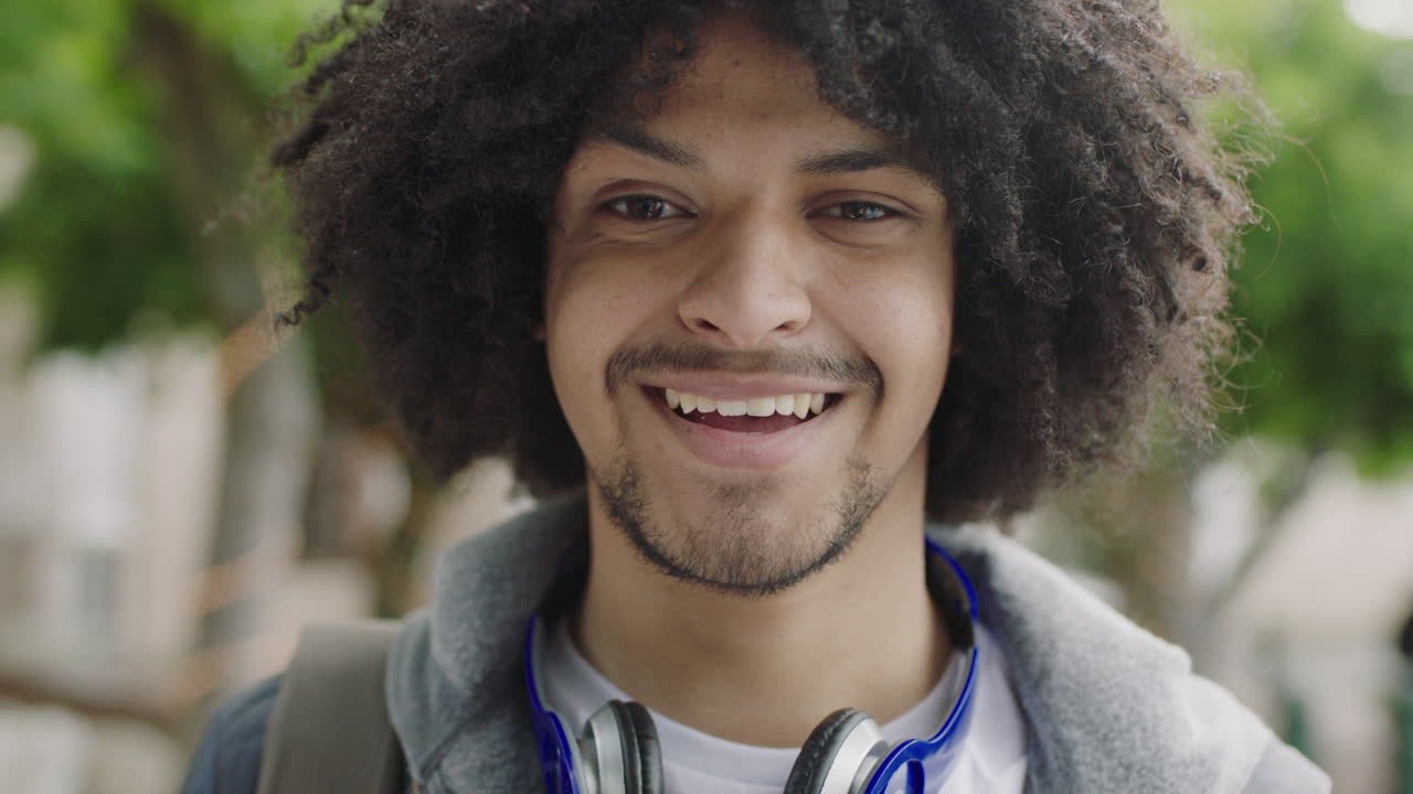 close up portrait of young mixed race student man laughing happy looking at camera enjoying independent lifestyle in urban city trendy afro hairstyle