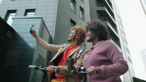 cheerful african american couple taking selfie with e-scooters in city