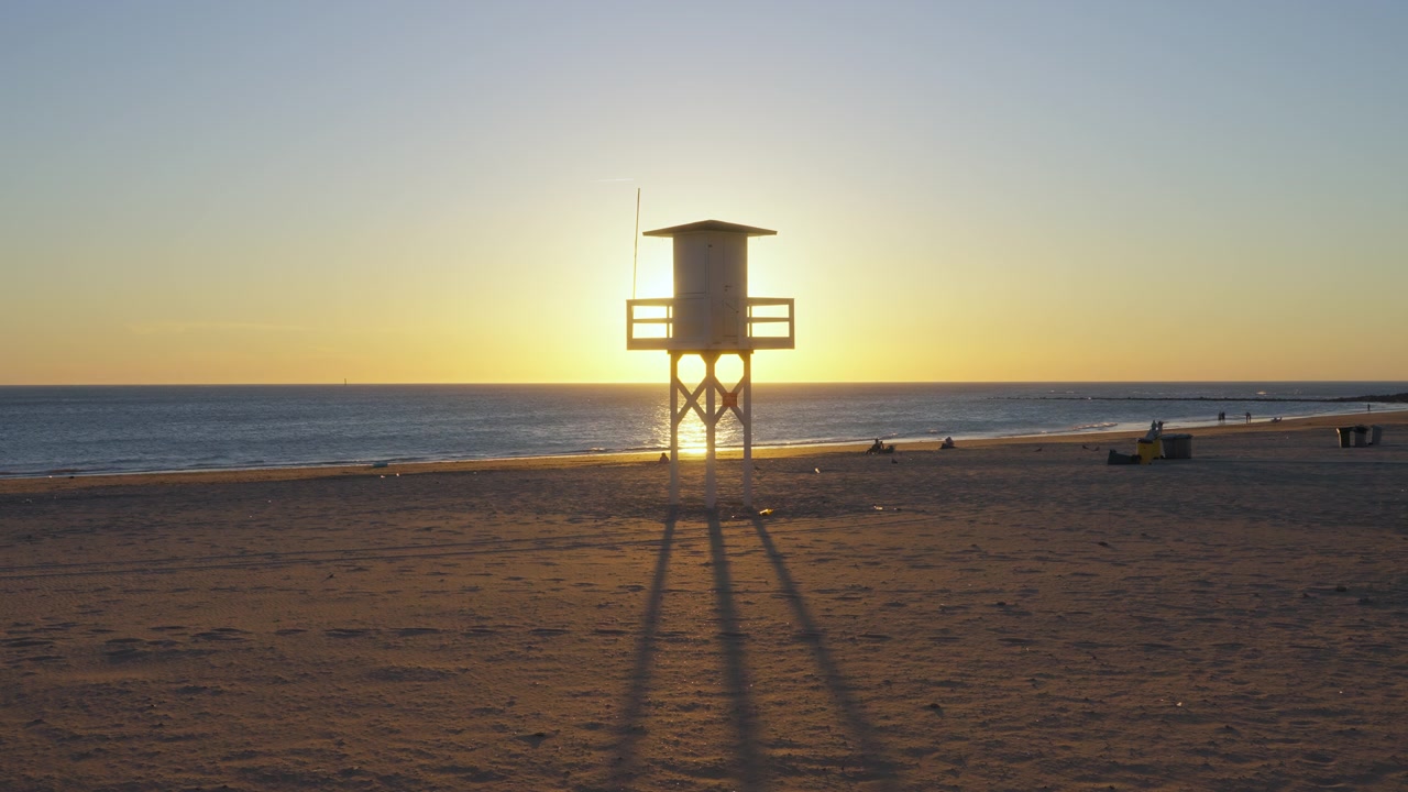 Toma amplia de una torre de vigilancia de socorristas con el sol brillando detrás, Chipiona, Cádiz, España.