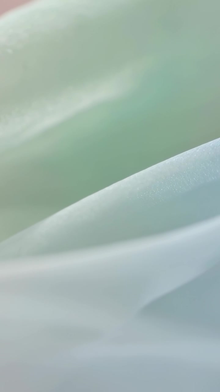 垂直影片：鏡頭移動，展現攝影棚內柔和薄荷綠布料的褶皺和質感