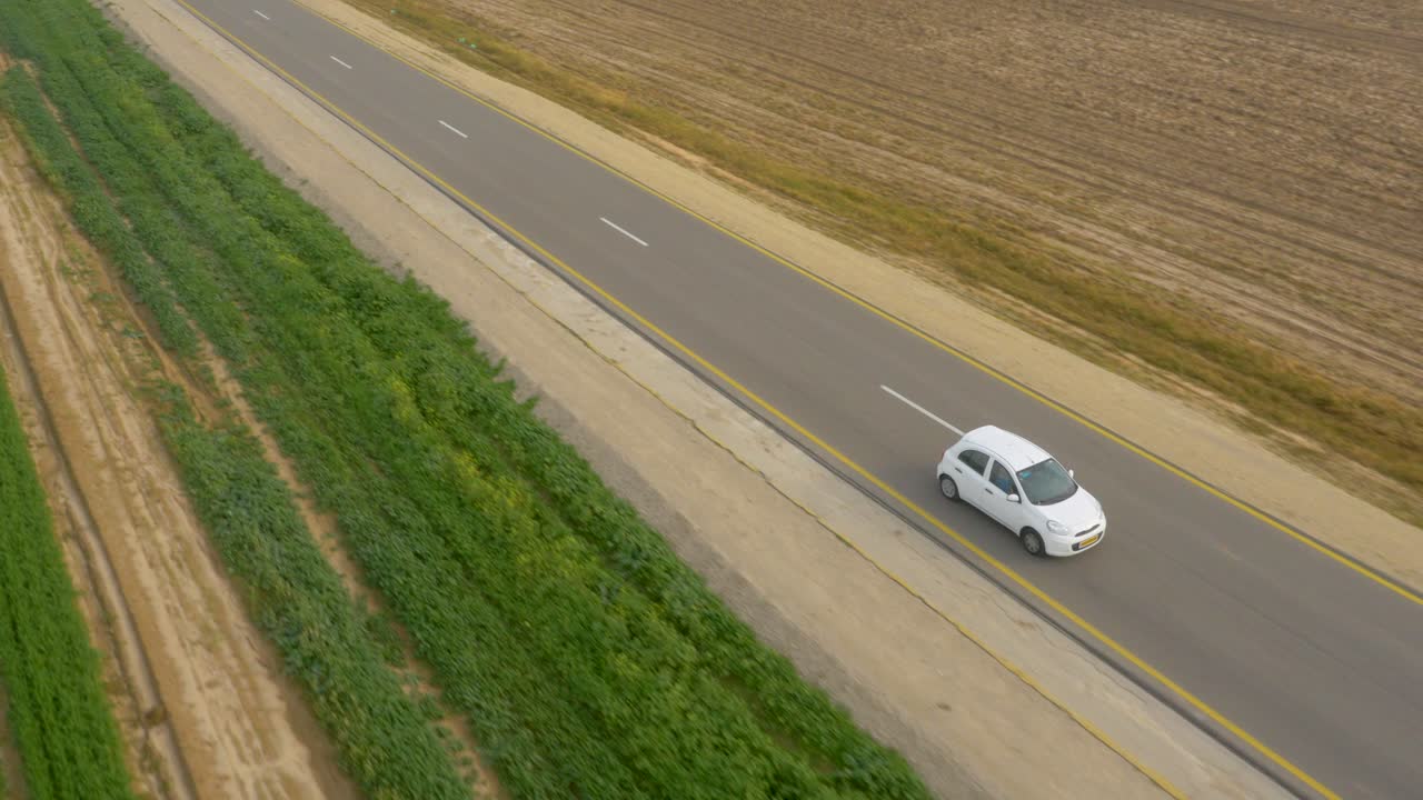 Aerial tracking small car driving on sealed road between agriculture crop fields
