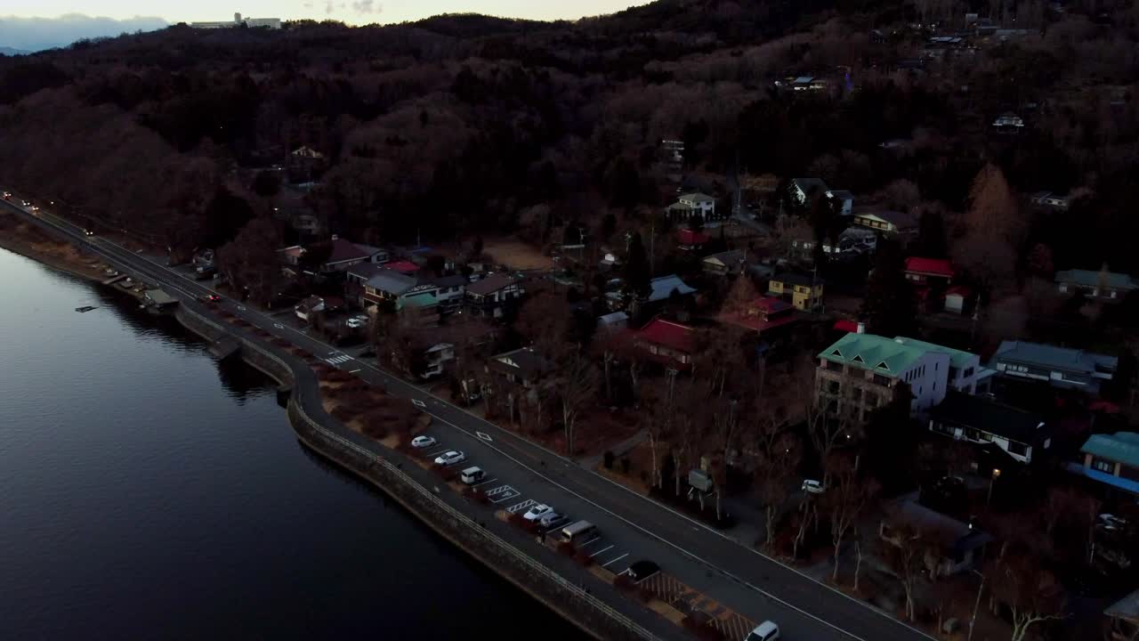 Tusmørke over en fredfyldt flod med tilstødende vej og parkerede biler, boligområde med træer
