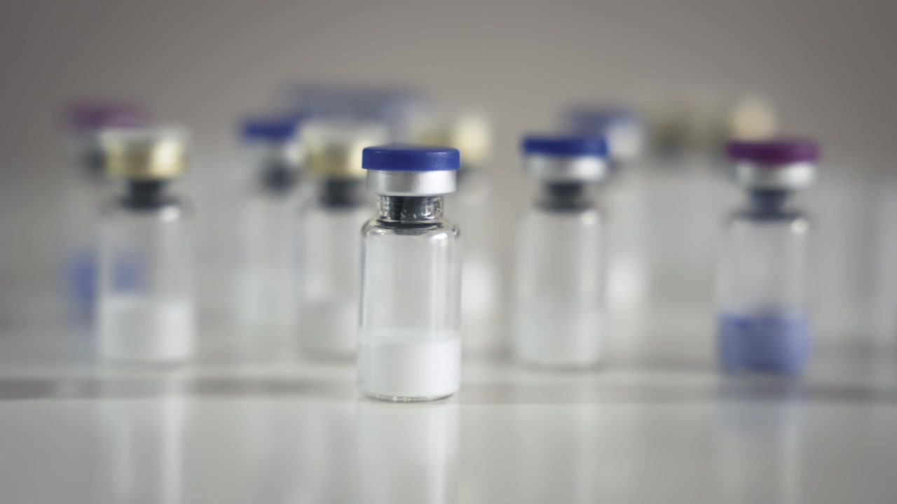 Tomada em dolly para a direita sobre múltiplos frascos farmacêuticos em uma mesa [Conceito de Peptídeo].