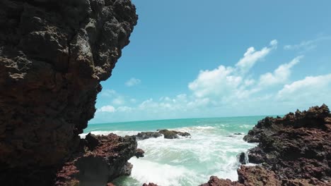 Tilt-up-handheld-action-camera-shot-of-small-waves-crashing-into-exposed-coral-rocks-during-low-tide-at-the-famous-tropical-Tambaba-beach-in-Conde,-Paraiba-Brazil-near-Joao-Pessoa-on-a-summer-day