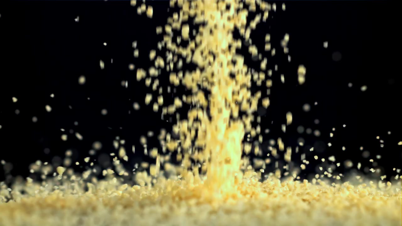 Chicchi di couscous dorati che cadono al rallentatore su sfondo nero
