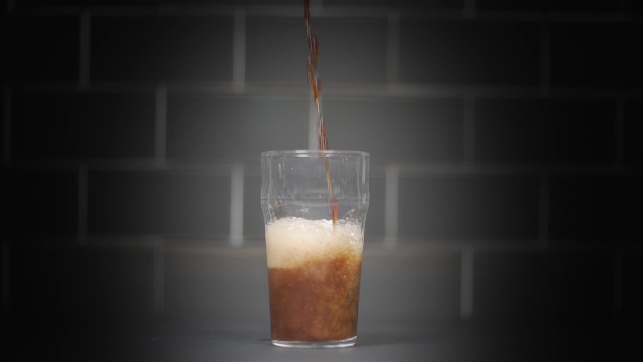 Wide shot of a glass on a counter with a dark stout beer being poured into it and then left to settle