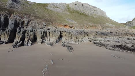 Luftaufnahme-Der-Meereshöhlen-Mit-Drängendem-Drohnenschuss-Und-Dramatischem-Küstenpfad-Am-Berghang-Im-Hintergrund-Auf-Der-Halbinsel-Gower,-Großbritannien-4k