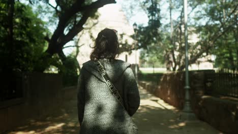 mujer caminando por un sendero iluminado por el sol en un parque sereno, luz moteada a través de los árboles, de vuelta a la cámara, entorno natural