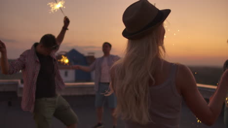 Rubia-Rusa-Con-Tres-Chicos-En-El-Tejado-Mueve-Maravillosamente-Sus-Brazos-Y-Su-Cuerpo.-Ella-Baila-Con-Sus-Amigos-En-Una-Tarde-De-Verano-Con-Una-Gran-Luz-De-Bengala.-Su-Cabello-Ondea-Maravillosamente-Con-El-Viento.