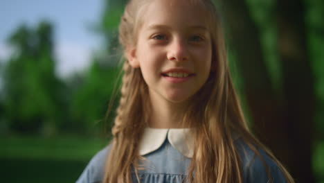 blonde girl posing alone with pigtail closeup. gentle kid look camera in park