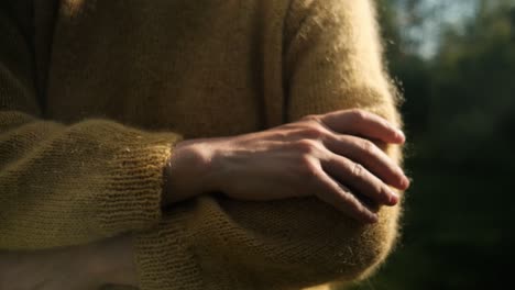 female hand touching soft, yellow sweater from wool in sunlight