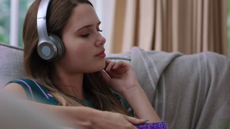 happy teenage girl listening to music wearing headphones relaxing on sofa at home texting with smartphone enjoying sharing lifestyle on social media