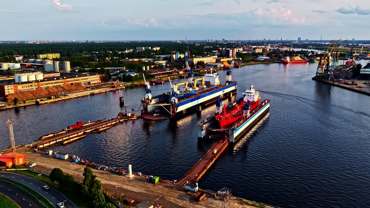 Drone establishing medium of industrial port terminal with docked cargo ships and cranes at sunset