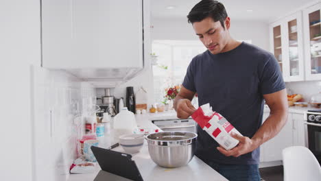 hombre milenario preparando una mezcla de pasteles siguiendo una receta en una tableta, añadiendo harina, cerca