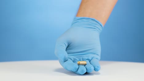 mano caucásica con guantes azules establece cápsula marrón claro, concepto de dolor
