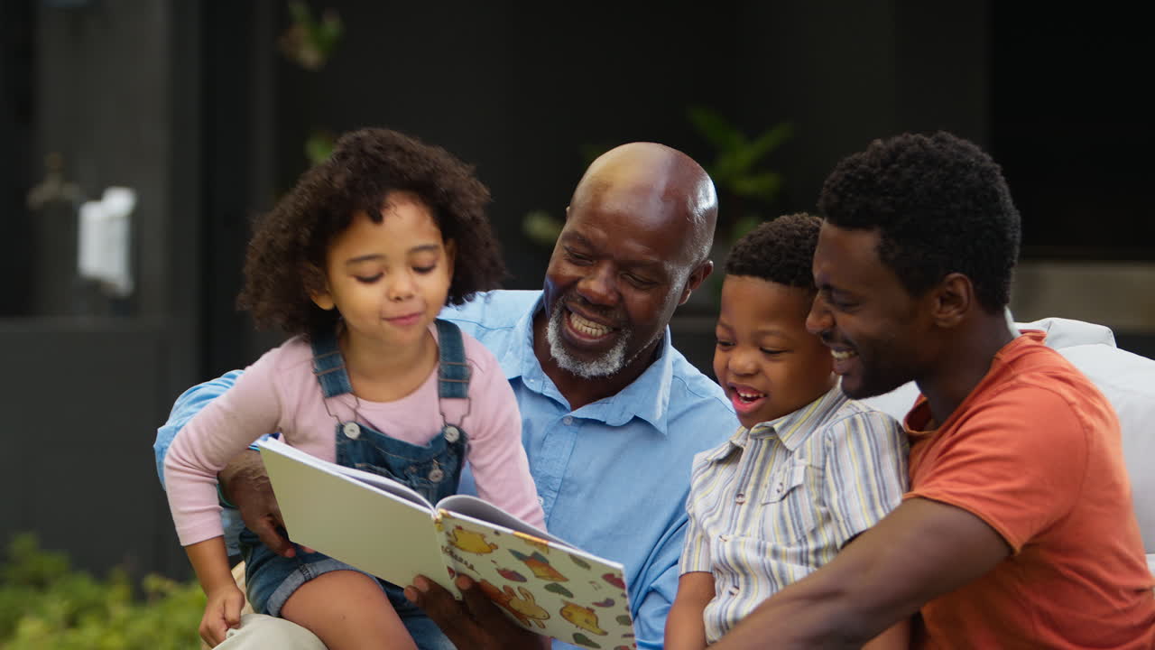Smilende familie i flere generationer læser bog i haven sammen.