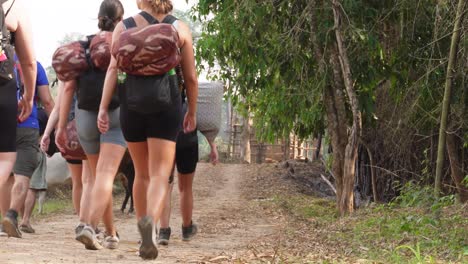 Un-Grupo-De-Mochileros-Jóvenes-Y-Aventureros-Está-Caminando-Y-Caminando-Hacia-Un-Pequeño-Pueblo-Con-Vacas-Al-Final-Del-Camino,-En-El-Norte-De-Tailandia-En-El-área-De-Umpang