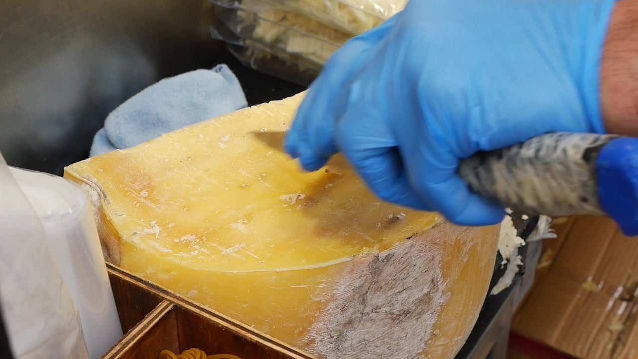 Person in Blue Gloves Scraping a Large Cheese Wheel