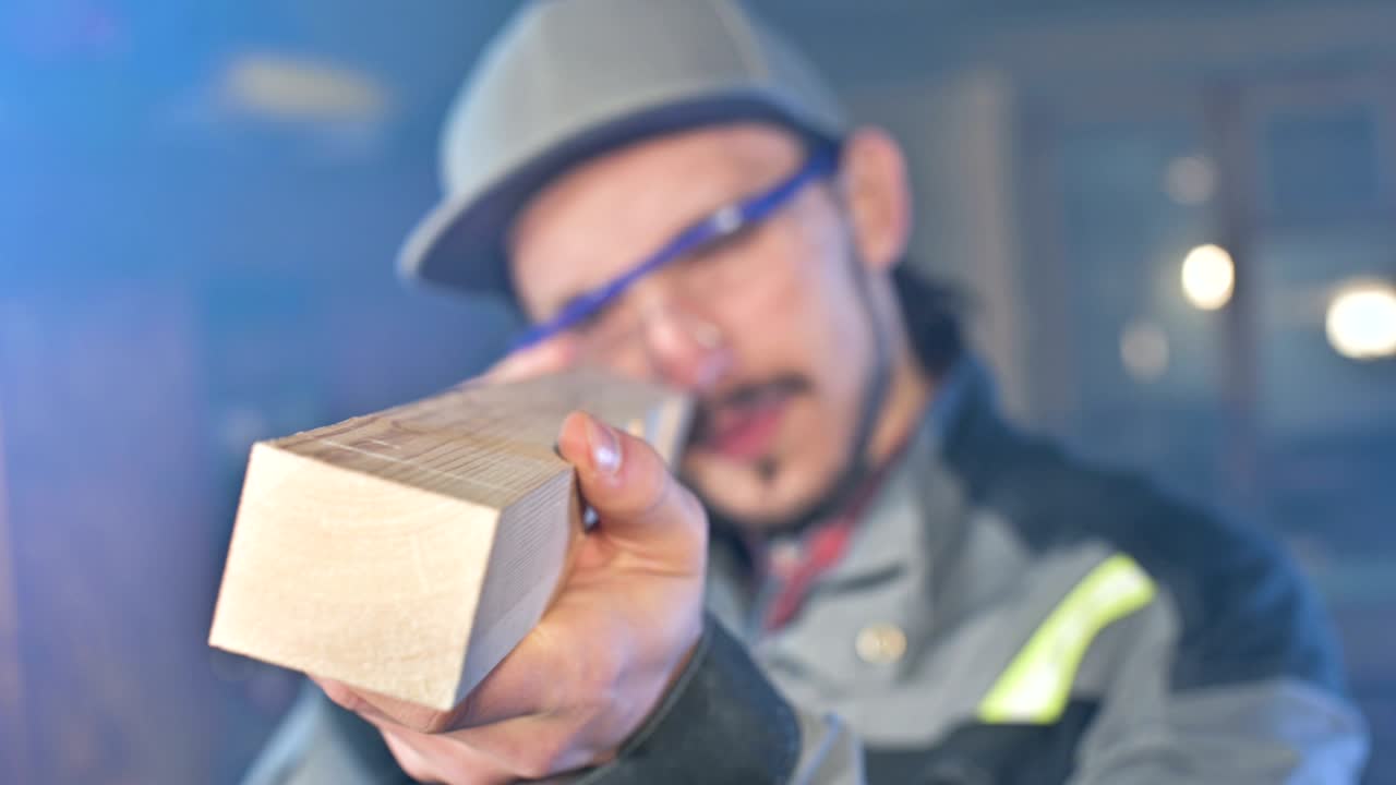 고글과 모자를 입은 집중된 젊은 수염이 있는 목공이 작업 조각을 확인합니다.