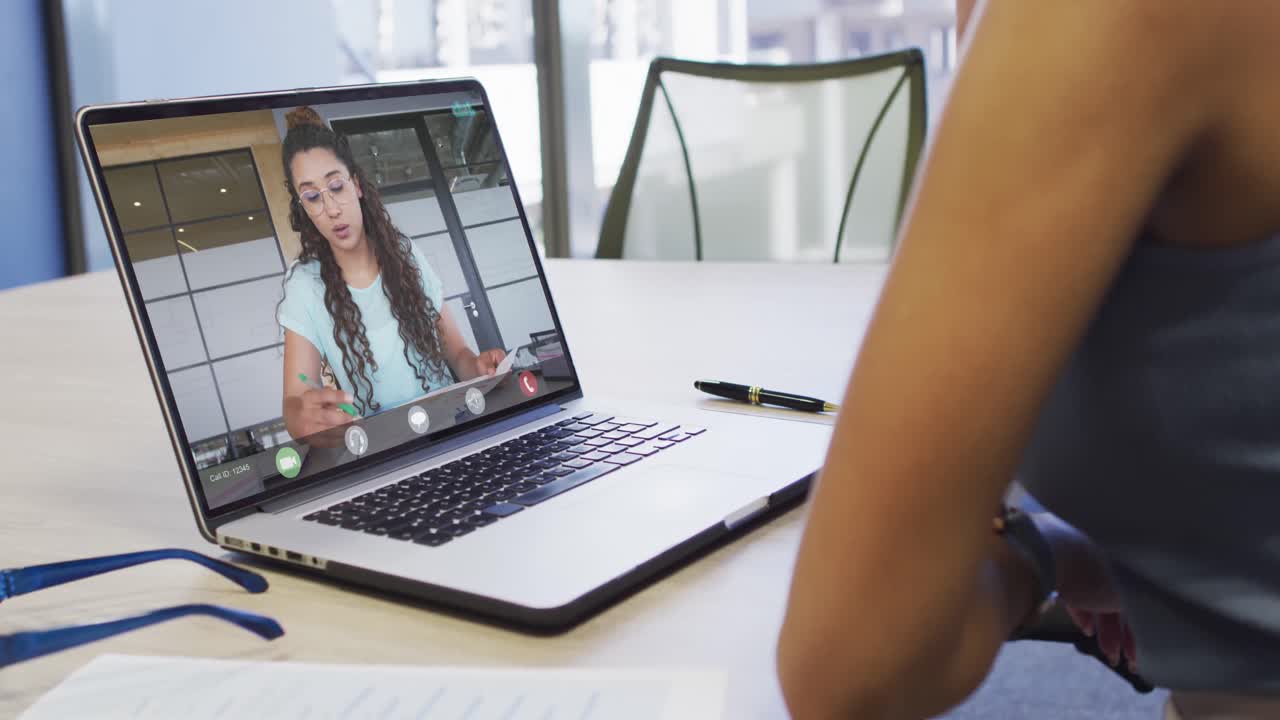 video de una mujer biracial haciendo una videollamada en un portátil con una compañera de trabajo caucásica