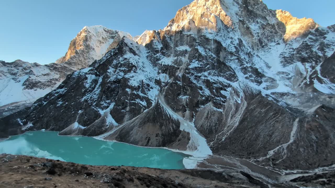 una lenta panorámica a través de un impresionante paisaje montañoso del himalaya bañado en la luz dorada del amanecer (alpenglühen), con un impresionante lago turquesa en primer plano, capturando la belleza de una mañana perfecta