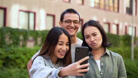 Grupo-De-Tres-Jóvenes-Amigos-Japoneses-Parados-Al-Aire-Libre,-Tomando-Divertidas-Fotos-Selfie-Y-Riendo-Juntos