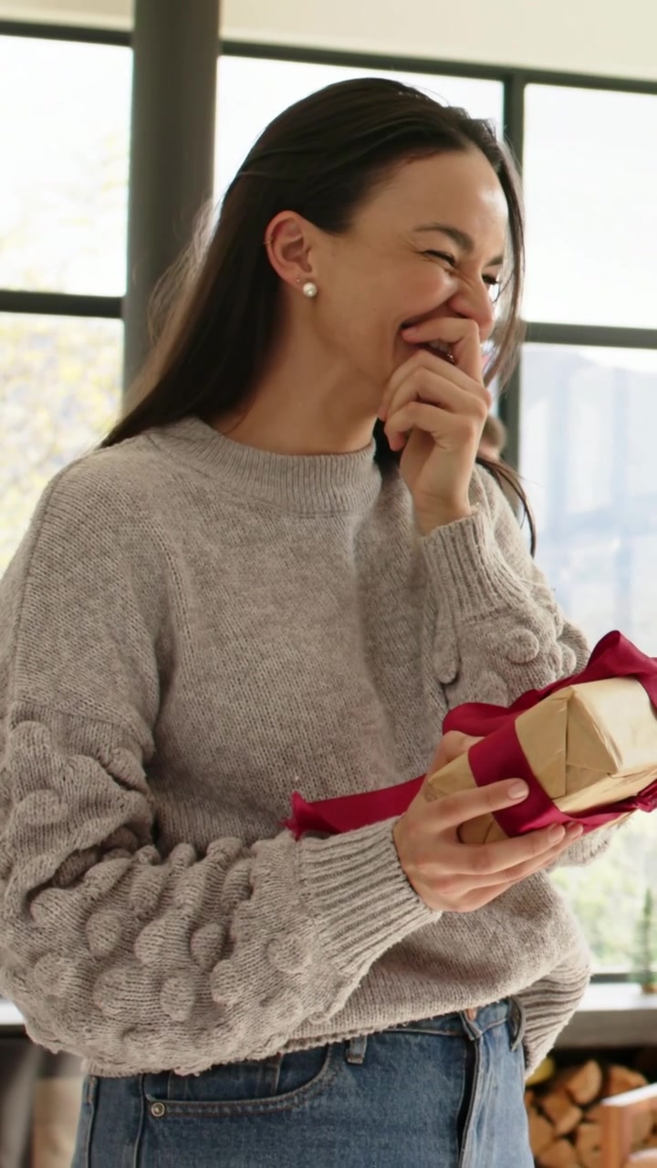 Video verticale: Donna con maglione grigio a casa, reagisce a un segnale fuori campo tenendo un regalo con nastro