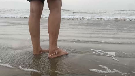 olas golpeando las piernas de una niña india de pie en la playa