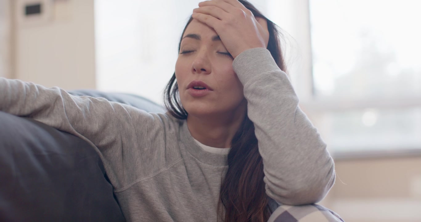 Donna seduta sul divano dopo lo stress, indossa una felpa grigio chiaro, abbassa la mano e si reclina.