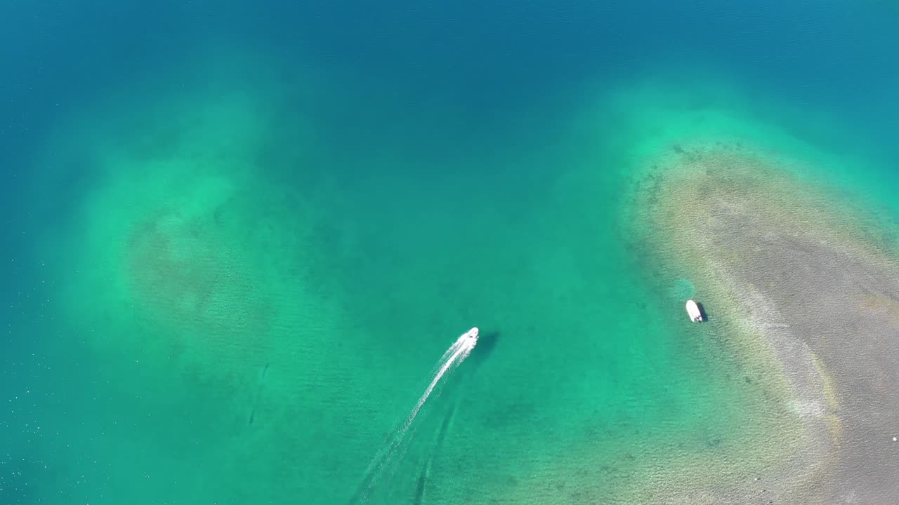 High aerial shot tracks motorboat rounding point, clear shallow water