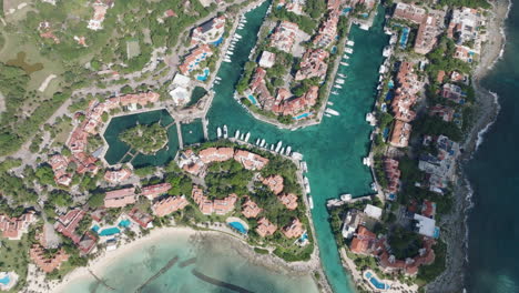 stunning bird's-eye view of a marina featuring yachts, holiday condominiums, and a serene sea with shadows of passing clouds