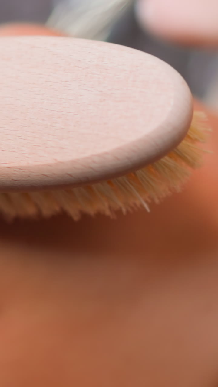 Young woman makes gentle massage moving anti-cellulite brush along arm and shoulder in shower at home skincare routine slow motion extreme closeup