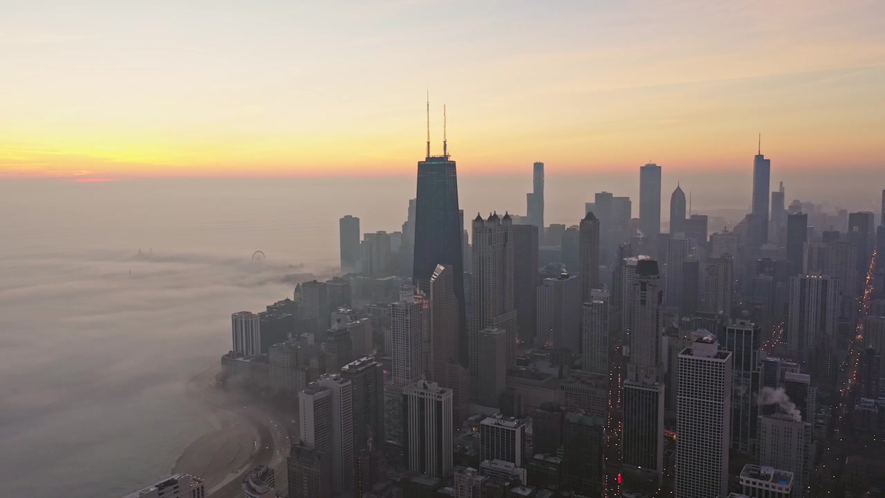 Filmagem aérea suave desliza pela direita sobre o horizonte de Chicago enquanto a névoa matinal cobre a margem do Lago Michigan sob a suave luz dourada do nascer do sol.