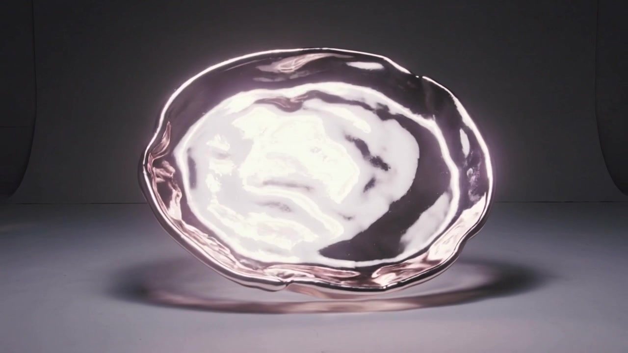 Turning rose-gold bowl starting lift above table, showing shifting specular highlights and shadow