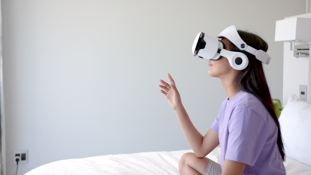 Using VR headset, woman sitting on bed and interacting with virtual environment, copy space