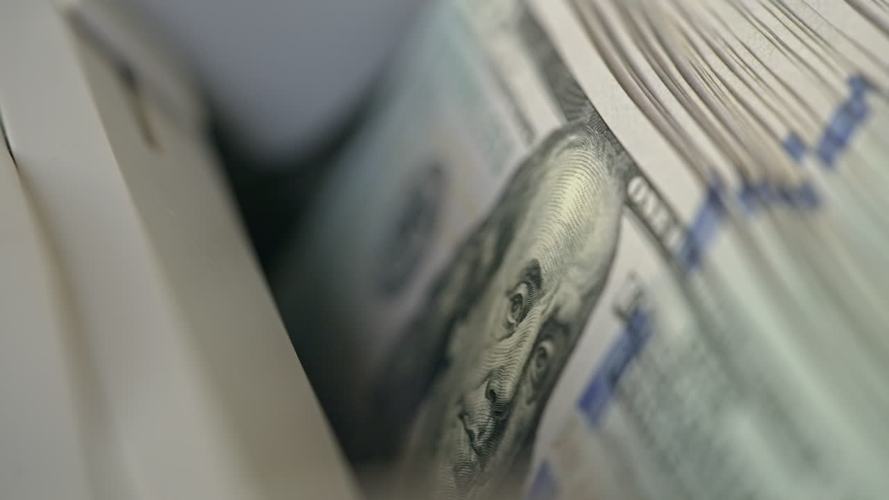 A number of hundred dollar bills with Benjamin Franklin portrait moving into money counting machine. Equipment for cash operations. Close up.