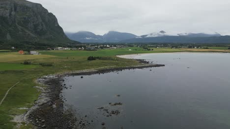 volando sobre el sendero costero en noruega con vista hacia las montañas y el océano abierto con casas rojas y hierba verde debajo y debajo del camino