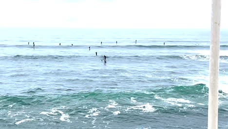 Ocean-Bliss:-Many-Surfers-Conquer-Three-Waves-Against-a-White-Sky,-Embracing-the-Endless-Swell