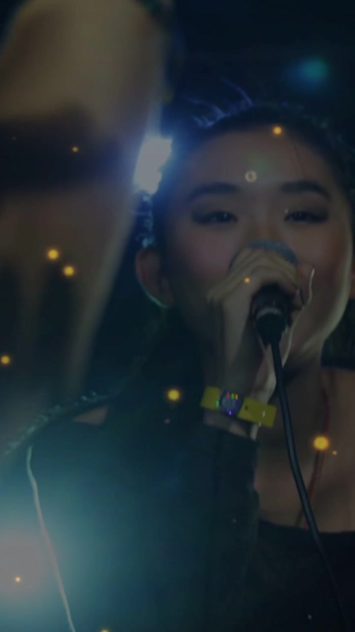 Vertical video: Female singer with mic singing music for fans, arm blocking view, gold dust overlay