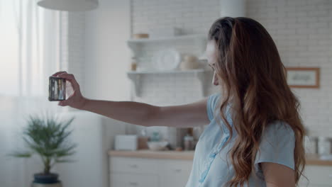 Joyful-woman-taking-selfie-photo-in-modern-kitchen.-Girl-posing-for-photo.