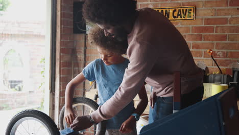 middle aged father helping his pre teen son use a spanner on the wheel of his go kart on a workbench in their garage, selective focus