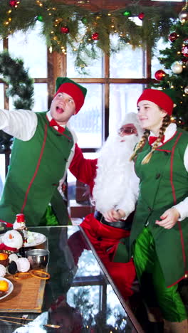 funny elves and santa in costumes in santa's residence. two elves and santa claus are posing to retro camera at christmas vertical video
