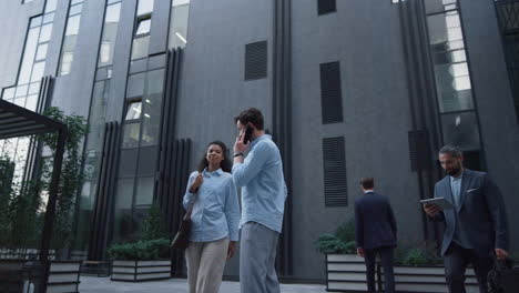 Businessman-speaking-phone-inspect-downtown-area.-Diverse-employees-passing-by