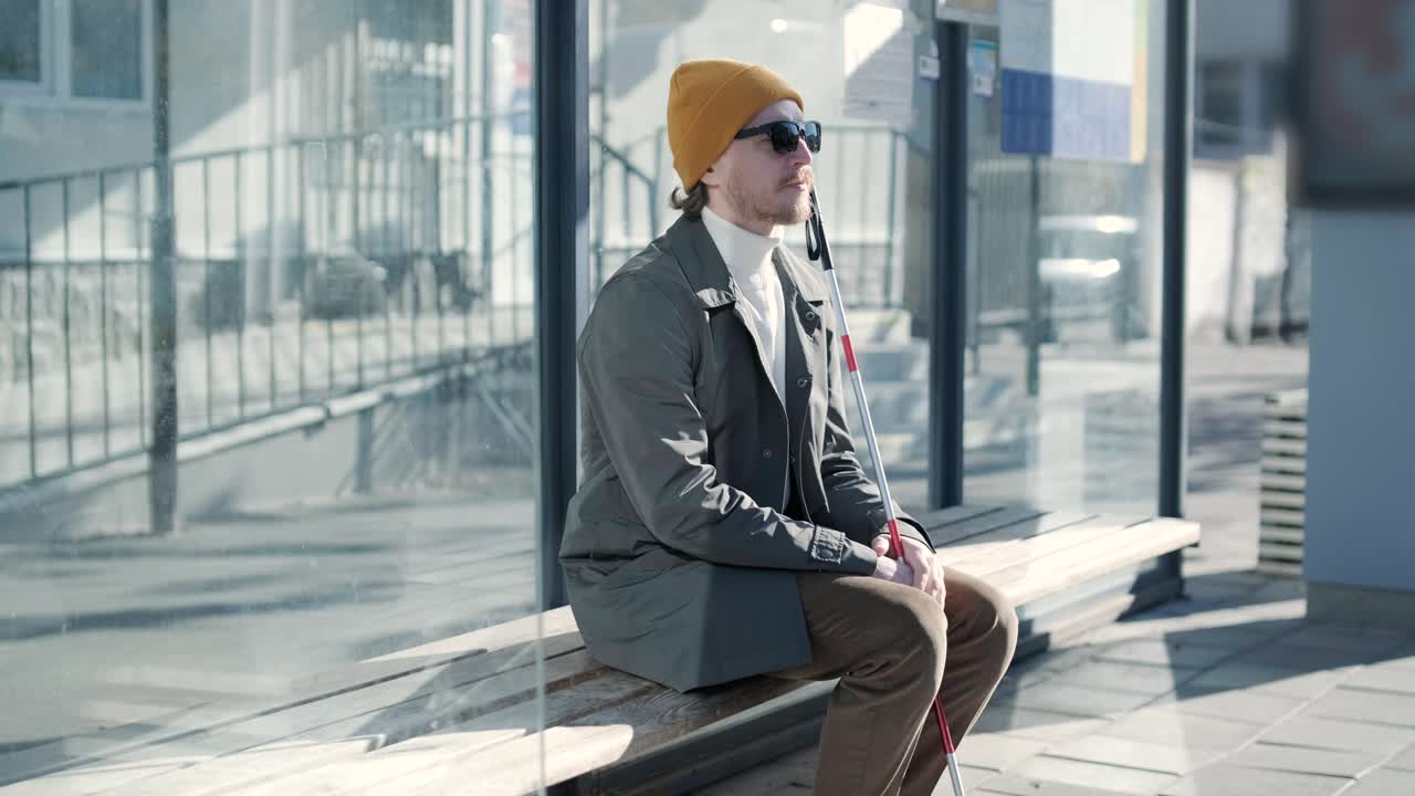 시내 버스 정류장에 앉아 있는 시각장애인.