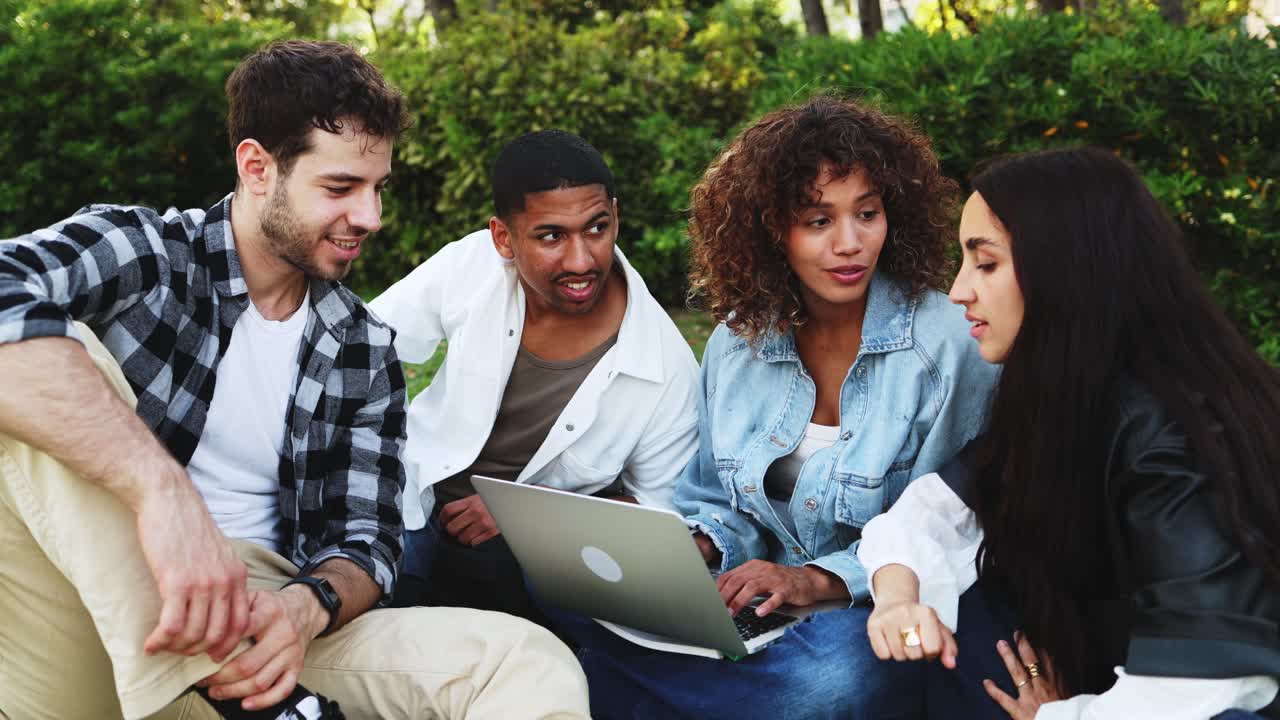 Gruppo diversificato di giovani adulti che collaborano al laptop in un parco