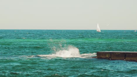 a sailboat, yacht on the horizon in the sea. splashing waves, ship in the background. breakwater.