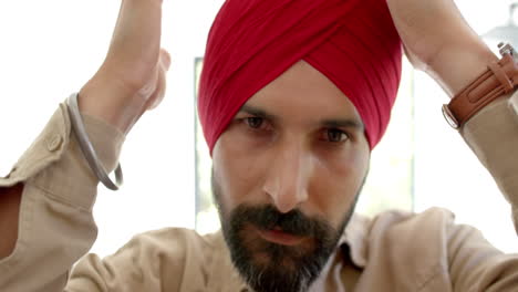 adjusting red turban, man looking serious and focused at home